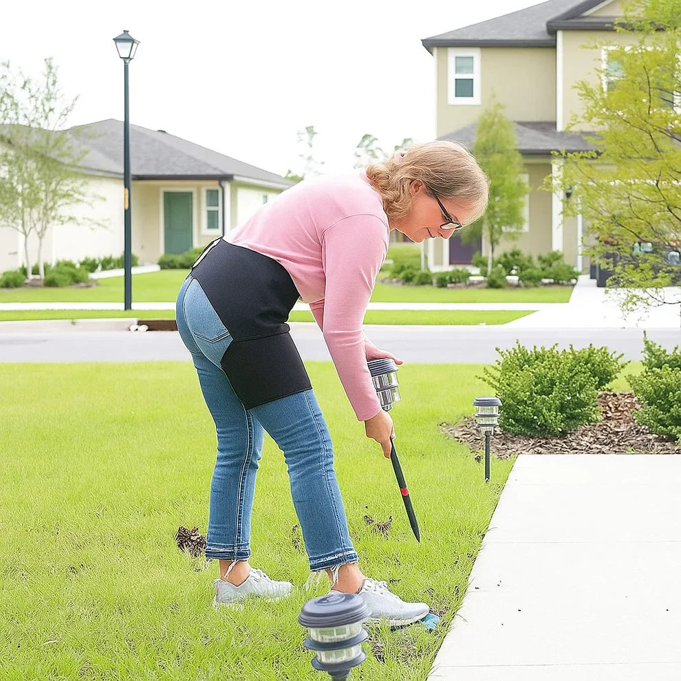 Person using a tool to adjust or install outdoor lights on a lawn.